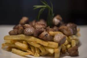 Un plato inspirado en el delicioso "Spa y masaje a lo japonés + menú de tapas en Madrid" incluye patatas fritas cubiertas con trozos de carne y una ramita de romero. - ForTwo - Planes para parejas