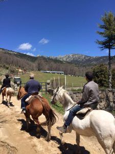 Gente disfrutando de un "Paseo a caballo por la sierra de Guadarrama con picnic para dos" en un camino de tierra a través de la pintoresca Sierra de Guadarrama bajo un cielo azul despejado. - ForTwo - Planes para parejas
