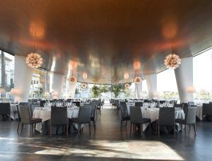El Restaurante Abades Triana se caracteriza por su espaciosa elegancia, con mesas redondas, sillas grises, grandes ventanales y lámparas de araña ornamentadas bajo un techo de madera que encarnan su encanto único. - ForTwo - Planes para parejas