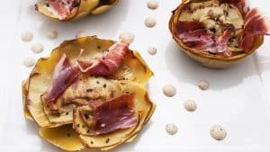 En el Restaurante La Rotonda del Hotel Westin Palace Madrid, saboree unas elegantes tartas de patata cubiertas con carne curada y semillas de sésamo, bellamente adornadas con puntos de salsa en un plato blanco impecable. - ForTwo - Planes para parejas