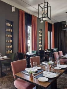 El sofisticado interior del Restaurante Ático en The Principal Madrid Hotel cuenta con mesas de comedor, altas cortinas naranjas y estantes adornados con velas contra paredes grises. - ForTwo - Planes para parejas