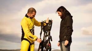 En Skydive Empuriabrava, durante el Salto tándem de paracaidismo, un instructor con un mono amarillo prepara el arnés de paracaídas de otro participante para una emocionante aventura al aire libre. - ForTwo - Planes para parejas