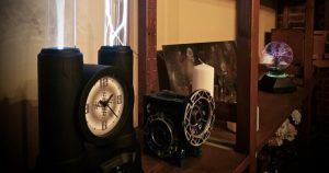En una habitación poco iluminada, la estantería exhibe una intrigante colección que incluye un reloj, una vela, elementos decorativos y una bola de plasma, que recuerda a la sala de escape Misión Oopart en Sevilla. - ForTwo - Planes para parejas