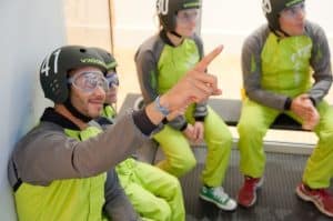 Cuatro personas con cascos y monos se sientan juntas, una señalando hacia adelante mientras se preparan para una emocionante Experiencia en Túnel de Viento en Madrid. - ForTwo - Planes para parejas
