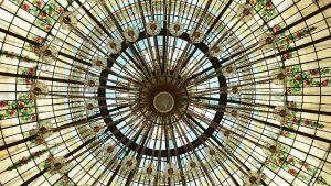 El hermoso techo abovedado de vidrieras del Restaurante La Rotonda en el Hotel Westin Palace Madrid presenta intrincados patrones circulares y exquisitos detalles florales. - ForTwo - Planes para parejas