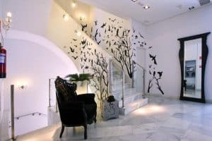 Una elegante escalera en el Hotel Dormirdcine Madrid, decorada con vinilos de pájaros y árboles, complementa perfectamente una silla negra ornamentada y un espejo alto, añadiendo un toque moderno al espacio. - ForTwo - Planes para parejas