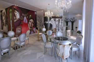 El elegante comedor del Hotel Dormirdcine Madrid exhibe murales artísticos en las paredes, mesas de cristal y sillas plateadas bajo brillantes candelabros de cristal. - ForTwo - Planes para parejas
