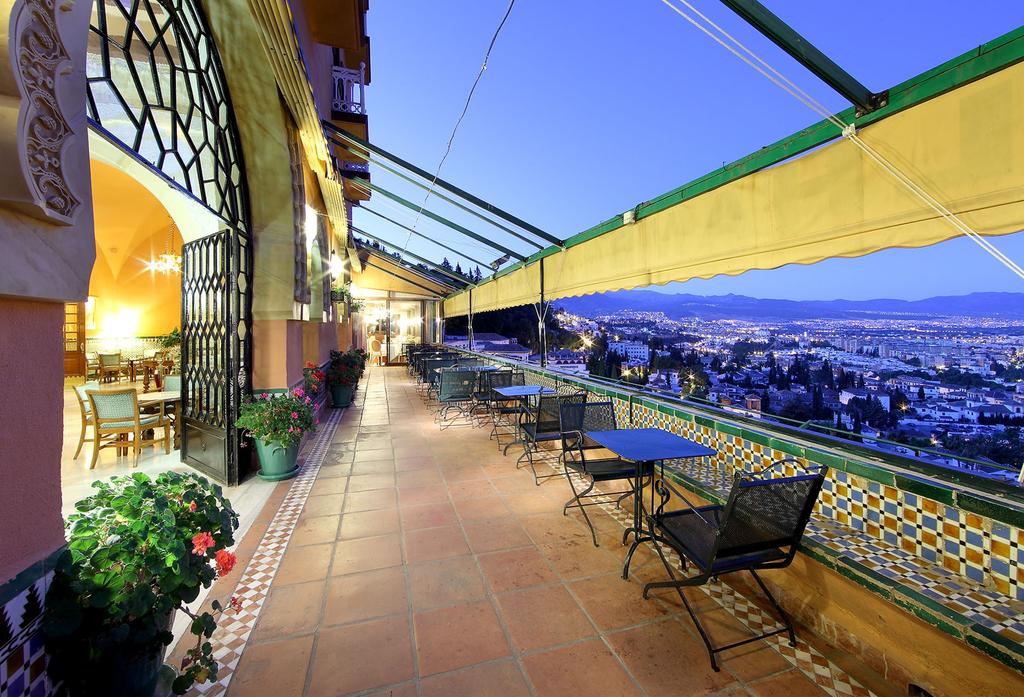 La terraza de la azotea del Hotel Alhambra Palace Granada cuenta con asientos con mesas y sillas y ofrece impresionantes vistas del paisaje urbano de Granada contra el cielo crepuscular. - ForTwo - Planes para parejas