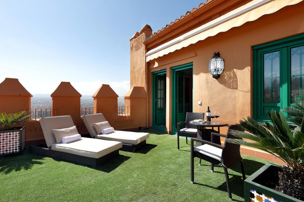 En la azotea del Hotel Alhambra Palace Granada, una terraza con tumbonas y una encantadora mesa con sillas y botella ofrece impresionantes vistas del paisaje urbano de Granada. - ForTwo - Planes para parejas