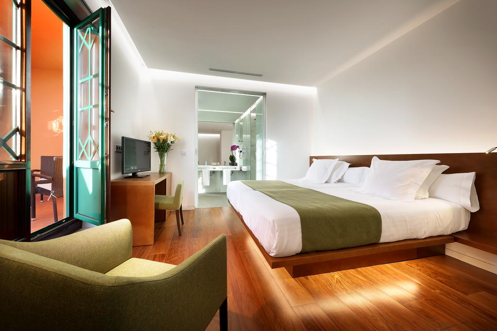 Alójese con elegancia en el Hotel Alhambra Palace Granada. Disfrute de una cama espaciosa, detalles en verde y suelos de madera. Salga a su balcón abierto para disfrutar de impresionantes vistas, a solo unos pasos del encanto histórico de Granada. - ForTwo - Planes para parejas