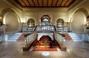 El Hotel Alhambra Palace Granada cuenta con un elaborado salón con intrincados arcos, escaleras, detalles dorados y una escalera central alfombrada que desciende con gracia, capturando el majestuoso encanto de Granada. - ForTwo - Planes para parejas