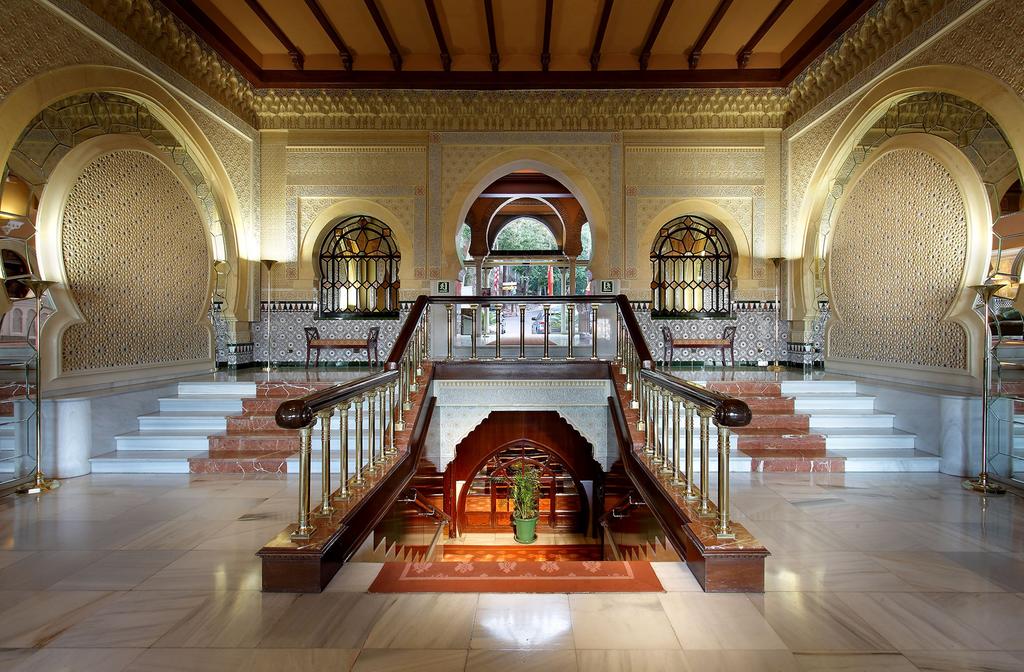 El Hotel Alhambra Palace Granada cuenta con un elaborado salón con intrincados arcos, escaleras, detalles dorados y una escalera central alfombrada que desciende con gracia, capturando el majestuoso encanto de Granada. - ForTwo - Planes para parejas