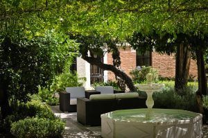 Ubicado en el encantador Hotel Hospes Palacio de los Patos Granada, este exuberante jardín cuenta con cómodos asientos junto a una fuente de un blanco inmaculado bajo un gran árbol. Captura a la perfección la esencia de Granada y es el lugar ideal para relajarse. - ForTwo - Planes para parejas