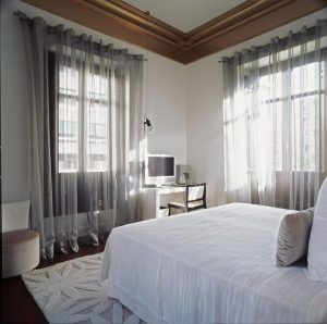 El Hotel Hospes Palacio de los Patos Granada ofrece un dormitorio luminoso con elementos de diseño moderno y minimalista como una cama, cortinas transparentes, un pequeño escritorio, silla y TV. - ForTwo - Planes para parejas