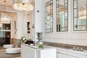 El Hotel Hospes Puerta de Alcalá 5 estrellas Madrid cuenta con un elegante vestíbulo con una decoración moderna, un mostrador de borlas blancas, lámparas de araña, espejos y exquisitos arreglos florales. - ForTwo - Planes para parejas