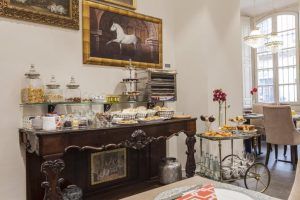 El elegante comedor del Hotel Palacete de Álamos Málaga ofrece un buffet de pasteles y aperitivos, realzado por una impresionante pintura de caballos y relucientes lámparas de araña. - ForTwo - Planes para parejas