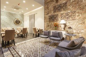 El moderno salón del Hotel Palacete de Álamos Málaga presenta un suelo de baldosas estampadas con sillas, un sofá, un gran reloj de pared y una pared de ladrillos decorativos. - ForTwo - Planes para parejas