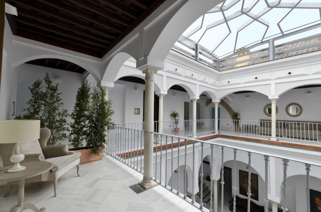 El Hotel Palacio de Pinello Sevilla cuenta con un elegante patio con techo de cristal, pasillos arqueados, cómodos asientos, una lámpara y plantas en macetas. - ForTwo - Planes para parejas