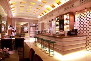 El Hotel Santo Domingo Madrid ofrece un bar elegante y moderno con asientos acolchados, detalles dorados e iluminación tenue. Su elegante decoración y sus sillas altas realzan el ambiente sofisticado. - ForTwo - Planes para parejas