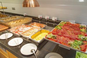 En el Hotel Santo Domingo Madrid, disfrute de un buffet con una variedad de carnes, huevos revueltos, pasteles y ensaladas adornadas bellamente presentadas en el mostrador. - ForTwo - Planes para parejas