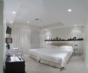 La habitación contemporánea del Hotel Santo Domingo Madrid ofrece dos camas individuales, elegantes obras de arte en la pared, escritorio, televisión e iluminación tenue. Las ventanas con cortinas a la izquierda realzan su elegancia. - ForTwo - Planes para parejas