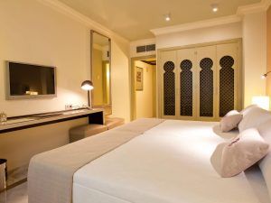 La habitación del Hotel Vincci Centro Granada incluye una cama grande, TV de pared, escritorio con lámpara y puertas de armario ornamentadas bajo una iluminación suave. - ForTwo - Planes para parejas