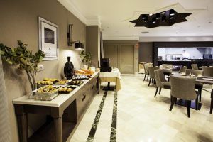 Una mesa de buffet con aperitivos en un elegante comedor del Hotel Vincci Centro Granada, con sillas grises y una decoración moderna, enclavado en el corazón de la ciudad. - ForTwo - Planes para parejas