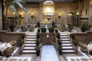 Explore el elegante patio interior del Hotel Vincci Centro Granada, completo con una lámpara de araña, palmeras, elegantes zonas de estar y una fuente de agua central: un refugio tranquilo en pleno corazón vibrante de la ciudad. - ForTwo - Planes para parejas