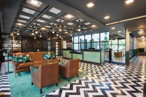 El vestíbulo del Hotel Room Mate Valeria Málaga presenta asientos de cuero marrón, iluminación geométrica, un suelo en zigzag y grandes ventanales de cristal. - ForTwo - Planes para parejas