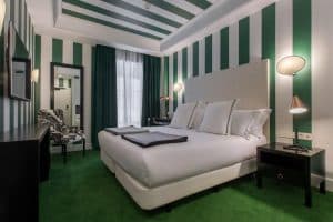 Descubra un oasis moderno en el Hotel Room Mate Valeria Málaga, con elegantes rayas verdes y blancas, una lujosa cama doble, elegantes muebles oscuros y una silla con un estampado único. - ForTwo - Planes para parejas