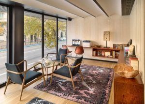 Una moderna oficina con grandes ventanales, sillas, una mesa de cristal, estanterías y elementos decorativos refleja el elegante diseño del Hotel H10 Puerta de Alcalá Madrid. - ForTwo - Planes para parejas
