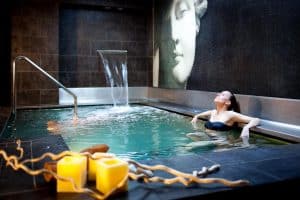 En el Hotel Wellington Madrid, una mujer disfruta de la moderna piscina cubierta que cuenta con una impresionante cascada y un mural artístico de fondo. - ForTwo - Planes para parejas
