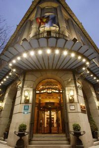 El Hotel Wellington Madrid cuenta con una entrada iluminada con un elegante toldo, elegantes columnas y dos banderas elegantemente colocadas sobre la puerta. - ForTwo - Planes para parejas