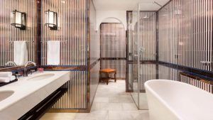 Un moderno baño de inspiración sevillana con bañera independiente, lavabos dobles, espejos, paredes rayadas y ducha con mampara de cristal combina el lujo con la elegancia del Hotel Alfonso XIII Sevilla. - ForTwo - Planes para parejas