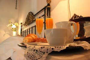 Disfrute de un desayuno de croissants, zumo de naranja y café elegantemente servido en una bandeja junto a una cama blanca adornada con flores en el Hotel Boutique Gar Anat Granada, situado en el encantador corazón de la ciudad. - ForTwo - Planes para parejas