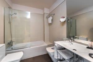 Descubra la elegancia de un baño moderno en el Hotel Boutique Gar Anat Granada, completo con una lujosa bañera, ducha, inodoro, espejo grande y lavabo elegante acompañado de artículos de tocador seleccionados. - ForTwo - Planes para parejas