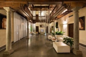 Descubra la grandeza del lobby del Hotel Boutique Gar Anat Granada, que muestra un diseño espacioso con techos altos, una elegante lámpara de araña, asientos blancos, majestuosas columnas y exuberante vegetación. - ForTwo - Planes para parejas