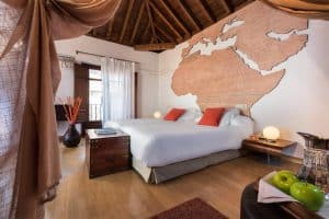 Una acogedora habitación del Hotel Boutique Gar Anat Granada en Granada cuenta con dos camas, un gran mapa del mundo en la pared y vigas de madera en el techo. - ForTwo - Planes para parejas
