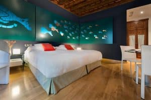 La habitación del Hotel Boutique Gar Anat Granada presenta una decoración moderna, con diseños artísticos de peces y tortugas en las paredes, una cama espaciosa con sábanas blancas y elegantes pisos de madera. - ForTwo - Planes para parejas