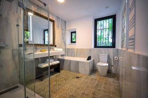 Disfrute de la elegancia de un espacioso baño de mármol en el Hotel Legado Alcázar (Sevilla), con ducha de cristal, bañera y un gran espejo. Una ventana llena de luz natural el sereno espacio, creando un refugio de lujo. - ForTwo - Planes para parejas