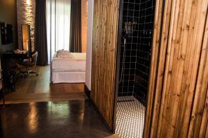 Disfrute de la comodidad y el estilo en una moderna habitación de hotel en Sevilla, con una pared con detalles de madera, ducha abierta y una cómoda cama. Un escritorio junto a la ventana ofrece el espacio perfecto para trabajar o disfrutar de la vista. Disfrute de un acceso sin problemas a la habitación del vestíbulo del hotel en Sevilla para una estancia inmersiva. - ForTwo - Planes para parejas
