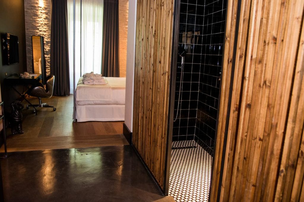 Disfrute de la comodidad y el estilo en una moderna habitación de hotel en Sevilla, con una pared con detalles de madera, ducha abierta y una cómoda cama. Un escritorio junto a la ventana ofrece el espacio perfecto para trabajar o disfrutar de la vista. Disfrute de un acceso sin problemas a la habitación del vestíbulo del hotel en Sevilla para una estancia inmersiva. - ForTwo - Planes para parejas
