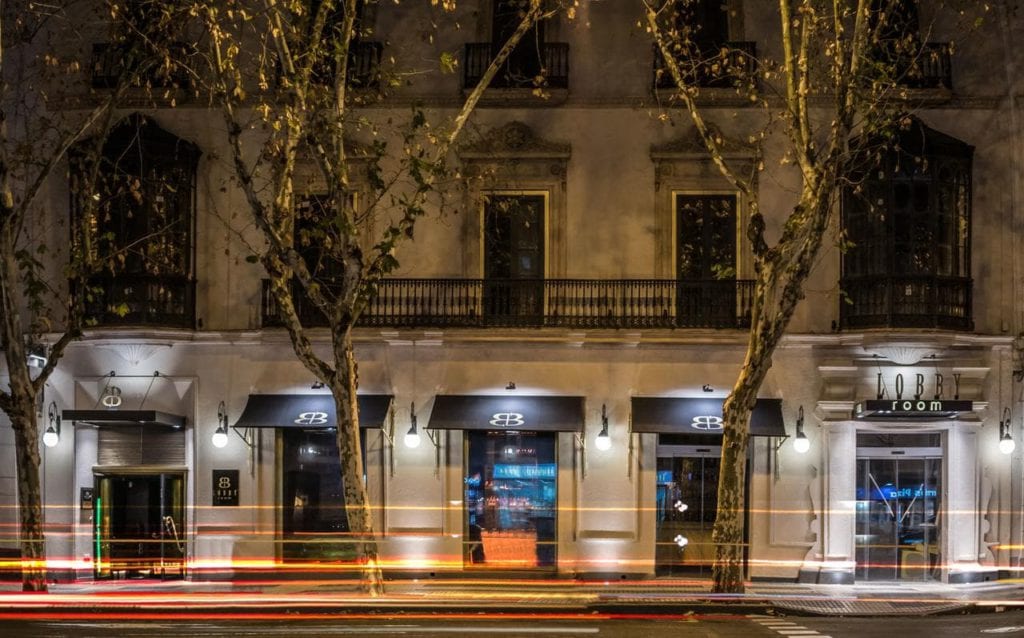 Vista de la calle del vestíbulo del Hotel Sevilla iluminado por la noche, con estelas de luz de los vehículos que pasan que añaden un primer plano dinámico. - ForTwo - Planes para parejas