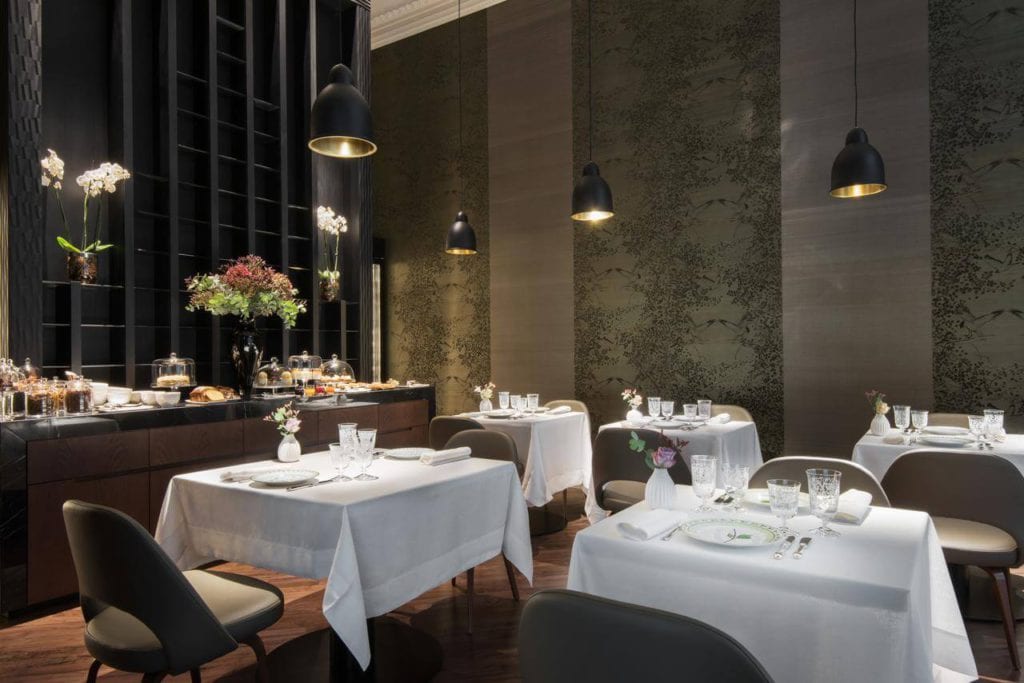 El elegante interior del Hotel Mercer (Sevilla) incluye mesas de comedor bajo luces colgantes ambientales y un buffet adornado con flores. - ForTwo - Planes para parejas