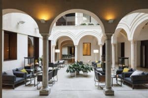 Experimente el elegante patio del Hotel Posada del Lucero Sevilla, donde los asientos modernos están enmarcados por arcos, florecen exuberantes plantas y la iluminación suave crea un ambiente acogedor. - ForTwo - Planes para parejas