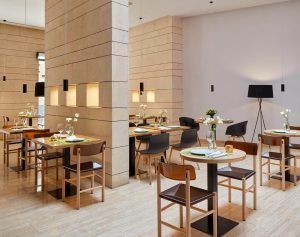 En el centro de Sevilla, el Hotel Rey Alfonso X cuenta con un moderno restaurante con mesas y sillas de madera, decoración minimalista e iluminación tenue. Elegantes centros de mesa florales realzan el ambiente. - ForTwo - Planes para parejas