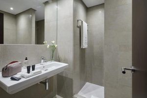 Experimente un moderno oasis de baño en el Hotel Rey Alfonso X Sevilla, equipado con un elegante lavabo blanco, espejo, ducha, lujosas toallas y artículos de tocador de alta gama para un toque de lujo. - ForTwo - Planes para parejas