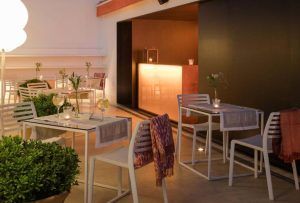 Un acogedor restaurante en el Hotel Rey Alfonso X Sevilla, con mesas y sillas blancas bajo una iluminación tenue, rodeado de exuberantes plantas. - ForTwo - Planes para parejas