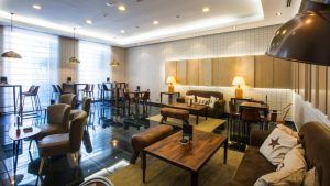 El salón del Hotel Vincci Selección Posada del Patio Málaga cuenta con sillas de cuero, sofás, mesas de madera, iluminación suave y una moderna pared con diseño de cuadrícula. - ForTwo - Planes para parejas