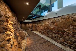 Situado en pleno corazón de Málaga, el moderno paseo del Hotel Vincci Selección Posada del Patio Málaga luce suelos de madera que contrastan con antiguas paredes de piedra, todo ello elegantemente iluminado bajo un tragaluz. - ForTwo - Planes para parejas